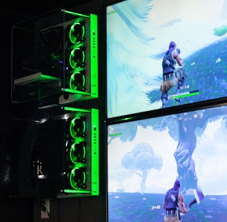 Two gaming monitors display an action scene from a video game featuring a character with purple hair in a lush outdoor setting. The gaming PCs are mounted on the wall with glowing green LED lights, and the room is dimly lit to emphasize the gaming setup.